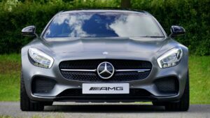 A front view of a gray Mercedes-AMG GT, with the AMG logo on the front bumper, parked in a grassy area.