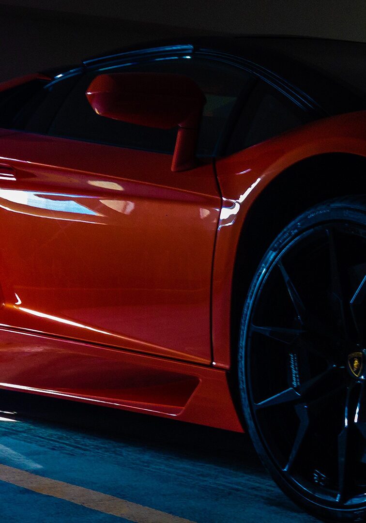 Luxury Lamborghini with black alloy wheels highlighted by dramatic lighting in an indoor parking area.