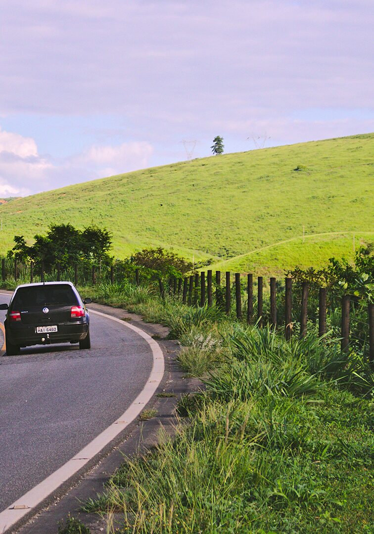 Car driving along a winding rural road surrounded by green hills and lush countryside.
