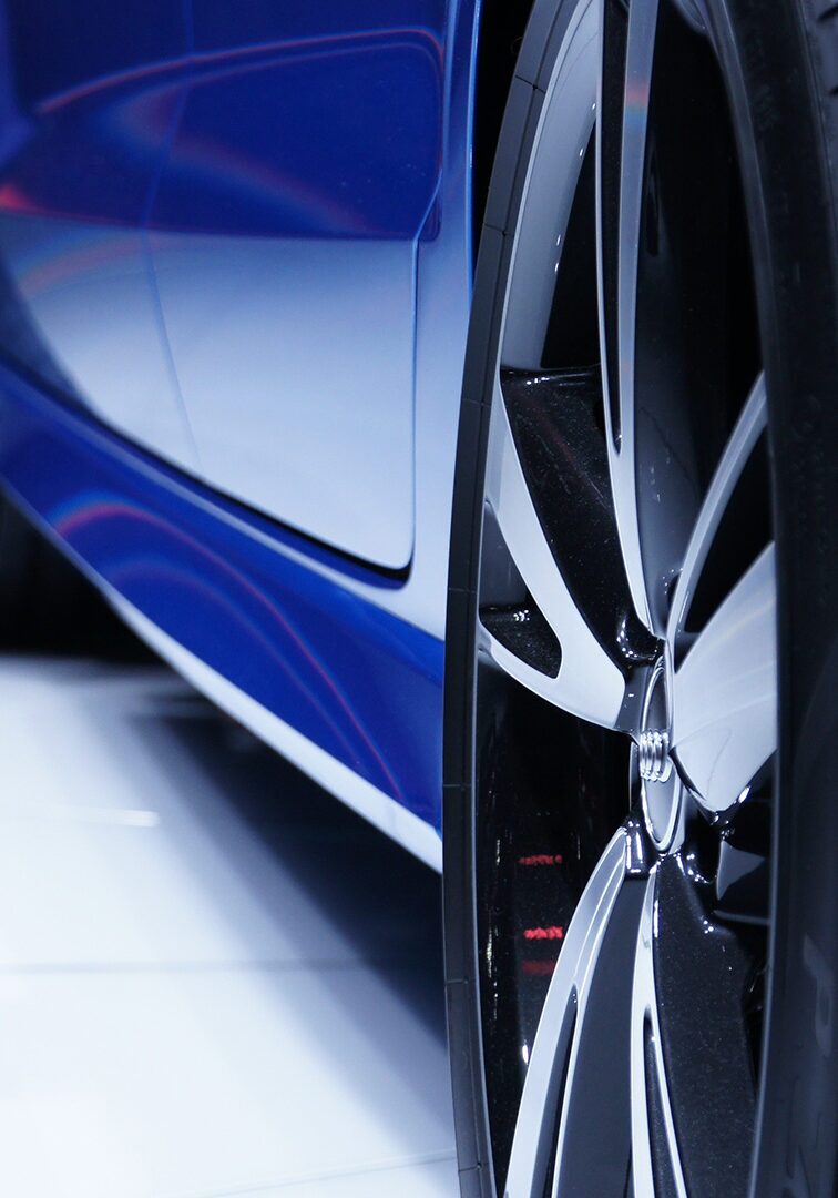 Close-up view of a blue luxury car's wheel and side panel with glossy reflections.